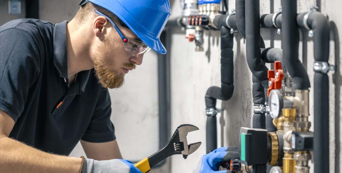 A man installs a heating system in a house and checks the pipes with a wrench. Adjusting heating valves in a residential building. A plumbing and heating technician works.