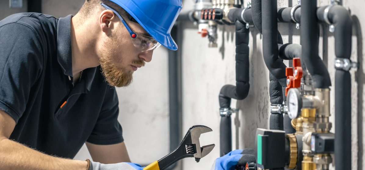A man installs a heating system in a house and checks the pipes with a wrench. Adjusting heating valves in a residential building. A plumbing and heating technician works.