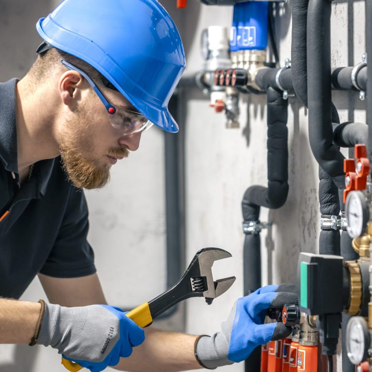 A man installs a heating system in a house and checks the pipes with a wrench. Adjusting heating valves in a residential building. A plumbing and heating technician works.